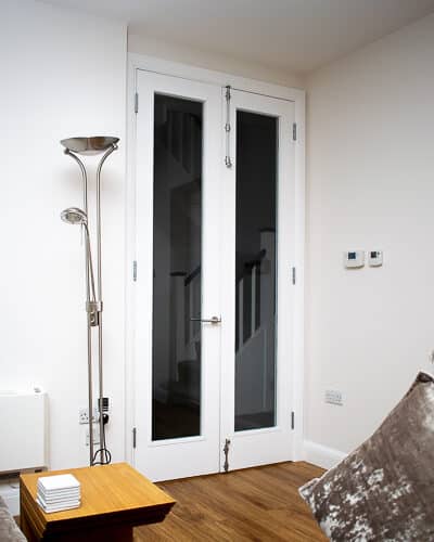 Tall white painted wooden internal fire doors with clear glass. Fitted onto hallway with satin chrome door furniture.