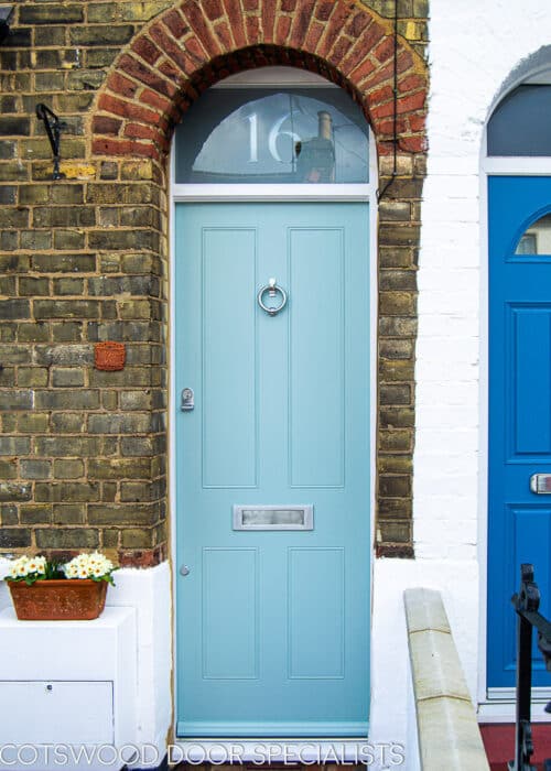 Traditional Victorian Front door fitted into a London terraced house. House is built with yellow stock bricks. Door frame has a fanlight that is fitted behind an arch. Door is painted a light blue colour and has tradtional butt and beaded panels. etched glass to transom with number