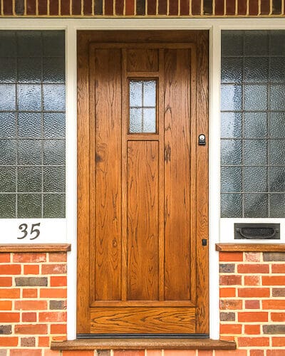 Tudor style door. 1930s style tudor door in natural wood. door has small piece of leaded glass and applied wooden ribbing. Sidelight frame is painted white and has leaded glass.