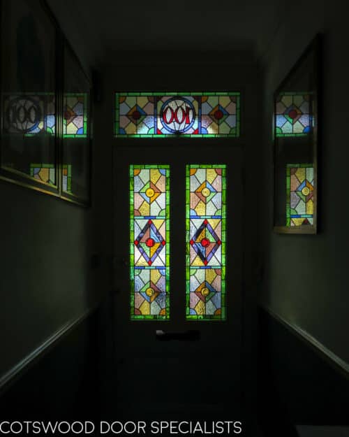 Victorian external door. Door and frame has ornate geometric stained glass. Door has 2 glass panels and one raised wooden panel. Painted finish Victorian door fitted in a storm porch. Polished chrome door furniture . Hallway shot showing off stained glass