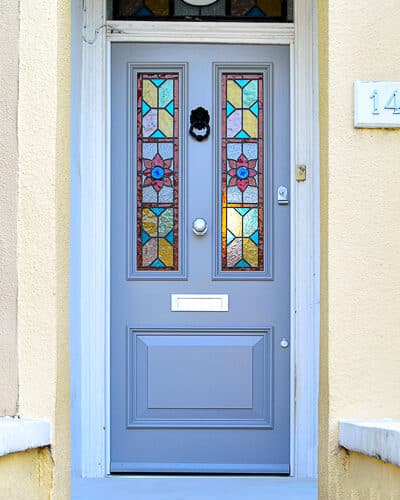 Victorian stained glass door. Gothic styled stained glass with bold colours fitted into a Victorian wooden door. Bold raised panel with decorative bolection mouldings. Door fitted into old white wooden door frame. Stained glass to transom above door with painted number
