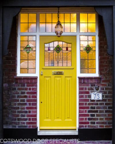 Yellow 1930s door. Yellow 1930s front door fitted into a large frame with stained glass surrounding door. Door has brass furniture. 1930s rose type stained glass to door and door frame. Fitted into a london home in a recessed arch.