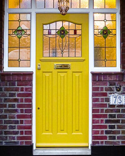 Yellow 1930s door. Yellow 1930s front door fitted into a large frame with stained glass surrounding door. Door has brass furniture. 1930s rose type stained glass to door and door frame. Fitted into a london home in a recessed arch.