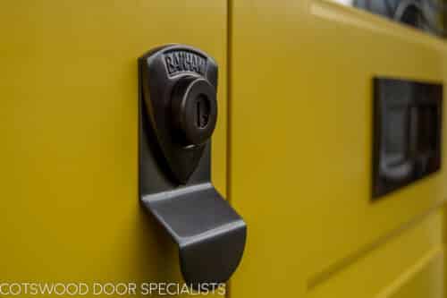 Yellow 1930s double doors with stained glass. Yellow painted wooden 1930s door fitted into a London red brick home. Orginal canopy made and fitted. Bronze door furniture. Detail shot of bronze banham lock