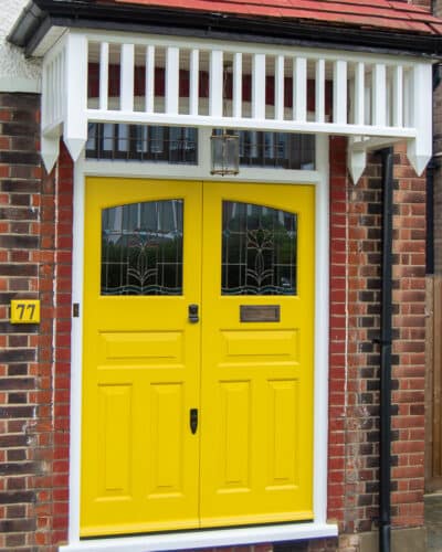 Yellow 1930s double doors with stained glass. Yellow painted wooden 1930s door fitted into a London red brick home. Original style canopy made and fitted. Bronze door furniture.