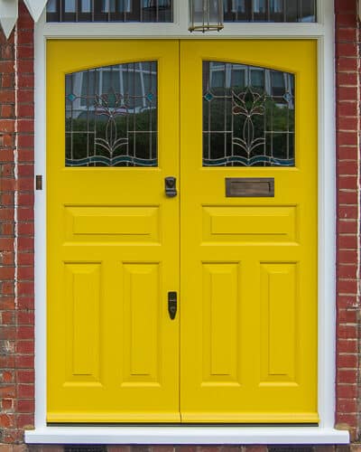 Yellow 1930s double doors with stained glass. Yellow painted wooden 1930s door fitted into a London red brick home. Original style canopy made and fitted. Bronze door furniture.