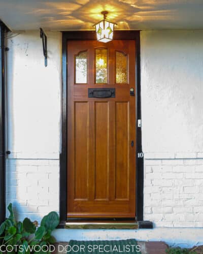 American Craftsman style front door. Accoya wooden door showing grain of timber. Tudor style black iron fitting and coloured glass. Gothic shape to head of door.