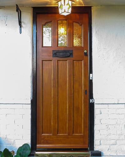 American Craftsman style front door. Accoya wooden door showing grain of timber. Tudor style black iron fitting and coloured glass. Gothic shape to head of door.