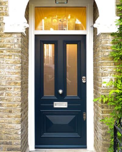 Beaded Victorian door. Victorian front door painted dark blue. fitted into a yellow stock brick london home. Door has 2 panels of glass and 1 raised cricket bat panel. The midrail around letterplate has a special horizontal bead detail replicating the original local joinery. Etched glass to door and number to frame
