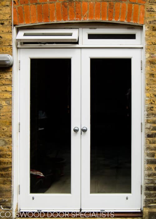 French door with fanlight. Fully glazed white wooden french doors fitted into a London stock brick home. Doors lead out to patio. Windows above doors are opening to provide ventilation