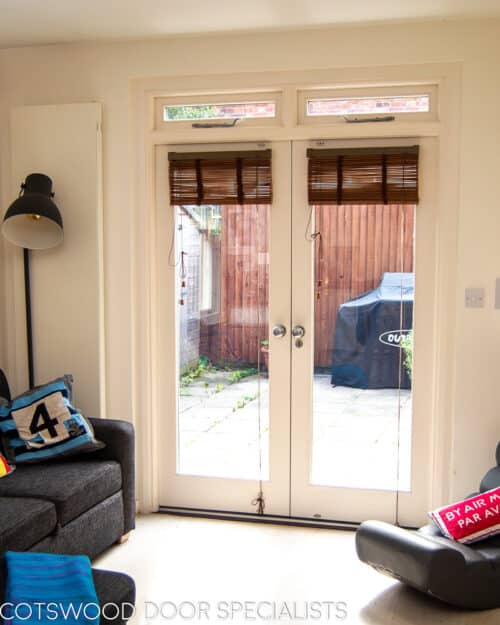French door with fanlight. Fully glazed white wooden french doors fitted into a London stock brick home. Doors lead out to patio. Windows above doors are opening to provide ventilation