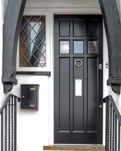 Mock Tudor 1920s door. Gothic style 1920s home with tudor style door. Door has multiple panels and has simple flat panels. Obscure glass to door to let some light in. House has black and white theme with black door
