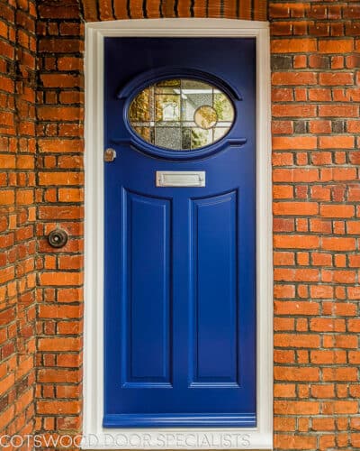 Oval 1930s Front door. Blue painted wooden front door fitted into red brick 1930s house. Door has contemporary styled stained glass. Satin chrome door furniture fitted with high security multipoint door lock