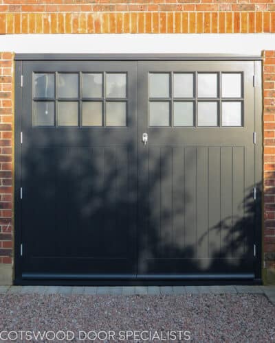 Side hung garage doors. Large grey painted 1930s style garage door with glazed top. Multiple panes of obscured glass divided with wooden glazing bar. Boarded bottom section to doors. Doors fitted with satin chrome door furniture