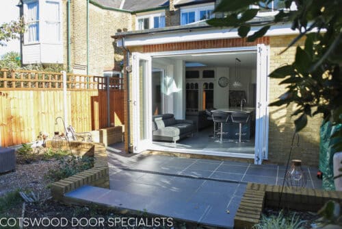 Sliding bi-fold door. 4 door external bifold door fitted into large kitchen extension. Full height glazed doors and complimenting fixed casement windows all painted white. Bifold doors open fully onto garden. Shot from patio