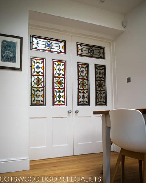 Stained glass Edwardian internal doors. Large pair of white painted wooden internal doors dividing kitchen diner and living room. Door have ornate stained glass with multiple panes.