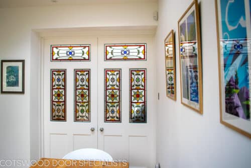 Stained glass Edwardian internal doors. Large pair of white painted wooden internal doors dividing kitchen diner and living room. Door have ornate stained glass with multiple panes.