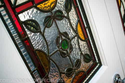 Stained glass Edwardian internal doors. Large pair of white painted wooden internal doors dividing kitchen diner and living room. Door have ornate stained glass with multiple panes. Closeup of stained glass
