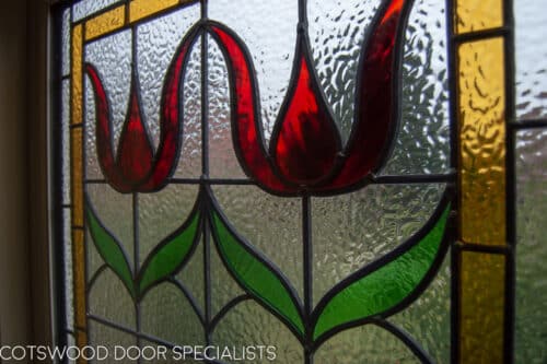 Stained glass casement window fitted onto landing in a large Edwardian home. Stained glass to window has flower motif in red colours. Window is painted white. Internal shot from hallway showing stained glass to window