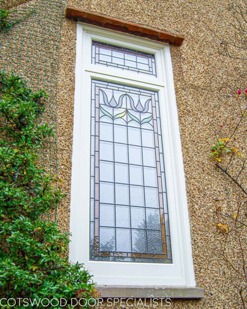 Stained glass casement window fitted onto landing in a large Edwardian home. Stained glass to window has flower motif in red colours. Window is painted white