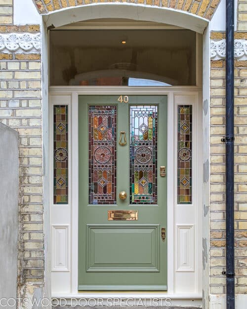 Victorian door with stained glass. Large Victorian front entrance with a double sidelight and transom door frame. Frame has fixed inset sash panels to copy the detail of the front door. Door and frame have geometric stained glass incorporating a York rose. Lots of colours to glass. Door is painted light green and has polished unlaquered brass door furniture. Fitted into a large london home with open storm porch