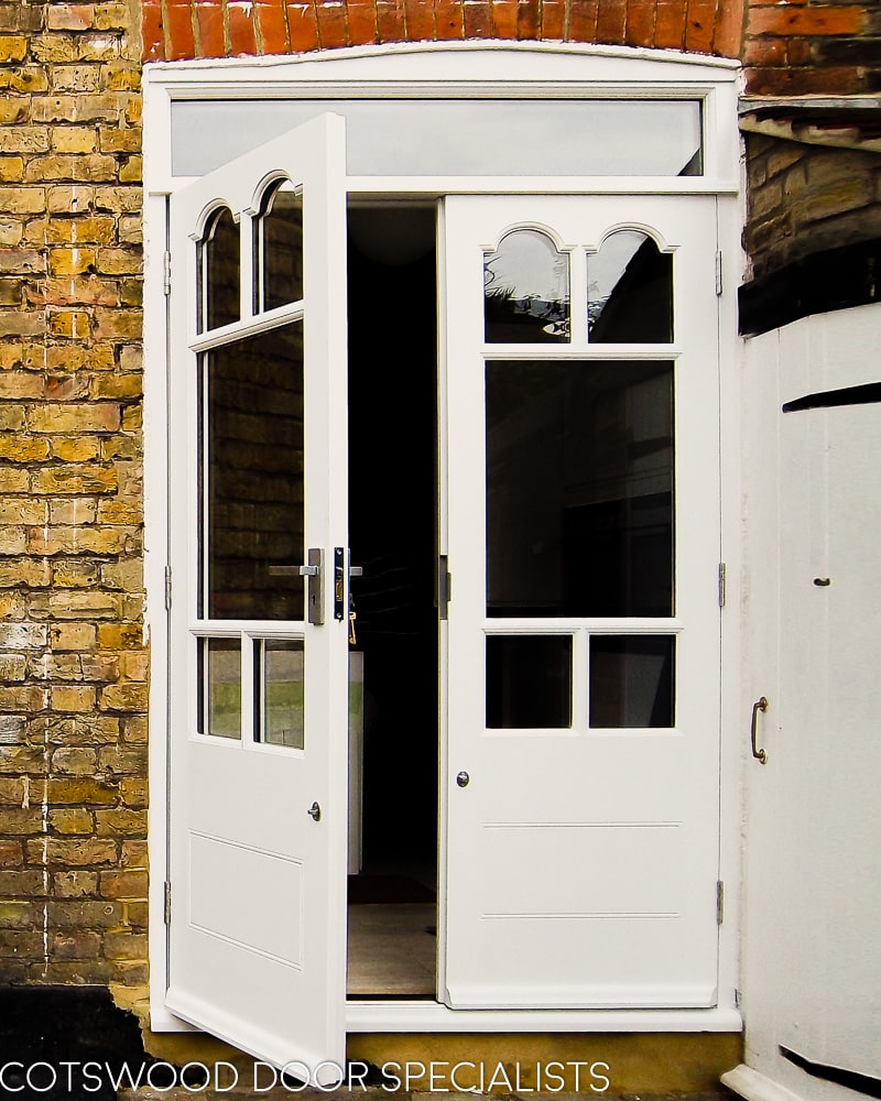 Edwardian french doors painted white. Glass in doors has decorative shapes matching original bay. Doors have a panelled bottom and are fitted into a yellow stock brick london home. Clear double glazed glass