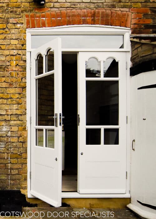 Edwardian french doors painted white. Glass in doors has decorative shapes matching original bay. Doors have a panelled bottom and are fitted into a yellow stock brick london home. Clear double glazed glass