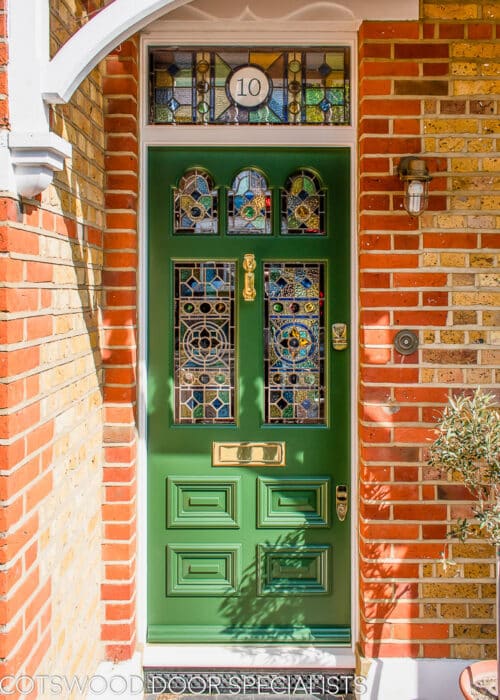 Forest green Edwardian front door. Replica of original Edwardian front door featuring traditional mouldings. Door has a decorative stained and leaded glass and also a number above the door. Forest green painted wooden door with polished brass door furniture featuring a doctor's knocker. Red and yellow london brickwork house with period canopy