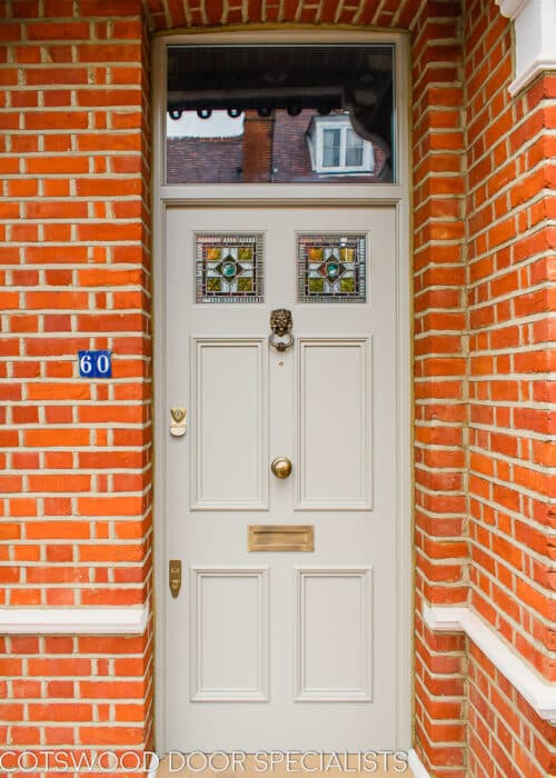 Leadlight Georgian front door. Six panel Georgian door with top panels glazed. Bottom wooden panels are flat with a period decorative moulding. Top panels have a leaded light with coloured glass and a rondel centrally. Door is painted lime grey to match the traditonal red brick and pointing surrounding the door. Antique brass door furniture including a lion door knocker.