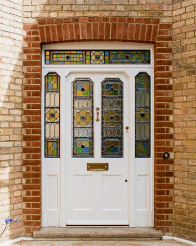 Intricate Victorian front door. Large front door and double sidelight frame with fanlight fitted into a large front entrance. Door has gothic shaped glass and chamfered moulding details. There are detailed scroll mouldings surrounding the panels. Panels have grooved boarding. The door has gunstock styles, of which are tapered to maximise light into hall. Traditional geometric stained glass featuring Muranese glass rolled with flowers, smooth waterglass borders, antique cathedral and also coloured rondels. Un-lacquered brass door furniture, of which is developing a patina.
