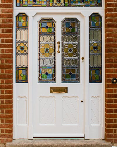 Intricate Victorian front door. Large front door and double sidelight frame with fanlight fitted into a large front entrance. Door has gothic shaped glass and chamfered moulding details. There are detailed scroll mouldings surrounding the panels. Panels have grooved boarding. The door has gunstock styles, of which are tapered to maximise light into hall. Traditional geometric stained glass featuring Muranese glass rolled with flowers, smooth waterglass borders, antique cathedral and also coloured rondels. Un-lacquered brass door furniture, of which is developing a patina.