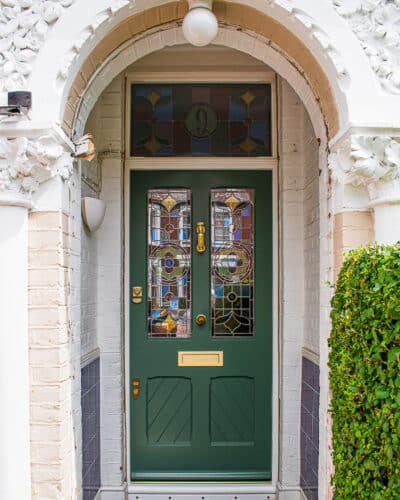 Stop chamfered Victorian front door painted green with satin brass door furniture. Stop chamfered mouldings to panels, glass and frame. Panels also have tongue and groove boarding set at an angle. Stained glass ring number and floral design