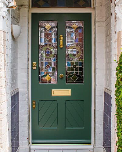 Stop chamfered Victorian front door painted green with satin brass door furniture. Stop chamfered mouldings to panels, glass and frame. Panels also have tongue and groove boarding set at an angle. Stained glass ring number and floral design