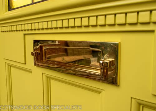 Sunrise 1930s front door. Door and frame painted yellow with an Art deco stained glass sunrise. Polished brass door furniture. Yellow and amber textured glass to sunrise with blue sky. Decorative shelf and apron to door with dental block. Closeup of letterplate and dental block detail