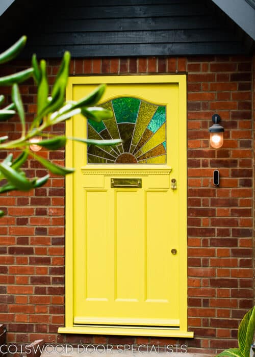 Sunrise 1930s front door. Door and frame painted yellow with an Art deco stained glass sunrise. Polished brass door furniture. Yellow and amber textured glass to sunrise with blue sky. Decorative shelf and apron to door with dental block. Photo showing door in new porch