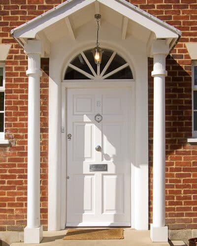White Georgian front door. Solid door with no glass painted white. Frame has a fanlight with radial wooden glazing bars. Door has decorative raised panels. Satin chrome door hardware.