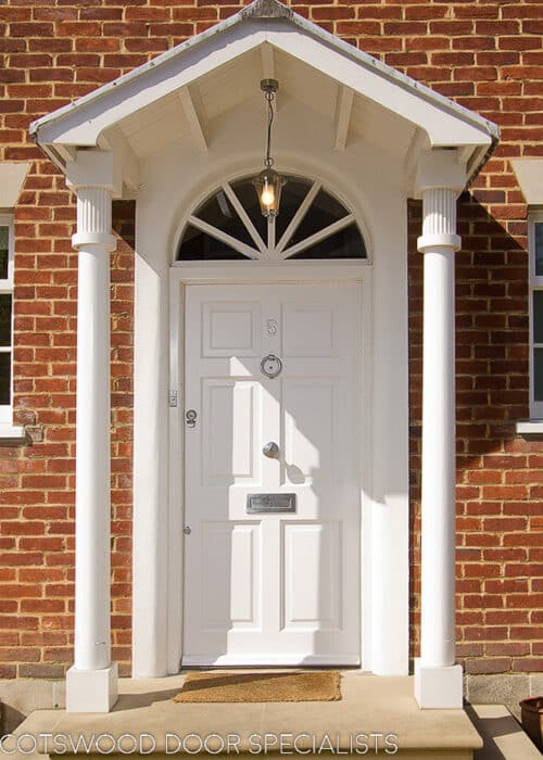 White Georgian front door. Solid door with no glass painted white. Frame has a fanlight with radial wooden glazing bars. Door has decorative raised panels. Satin chrome door hardware.
