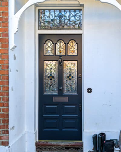 Classic blue Victorian door with shaped glazing. Stained glass design with leaves and beautiful colours. Decoraitve rondels as centre features in different colours. Number to transom panel. Door is a very dark blue and is fitted with bronze door furniture including banham locks.