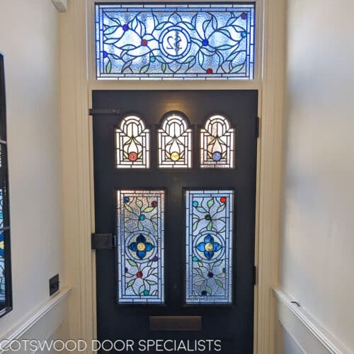 Classic blue Victorian door with shaped glazing. Stained glass design with leaves and beautiful colours. Decoraitve rondels as centre features in different colours. Number to transom panel. Door is a very dark blue and is fitted with bronze door furniture including banham locks.