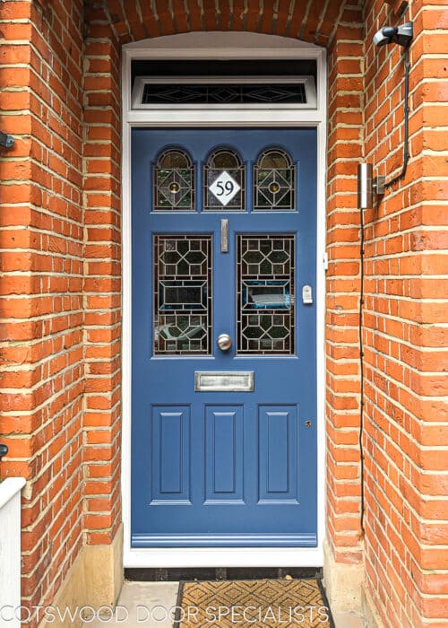 edwardian front door, fitted in a london red brick home painted brilliant blue RAL5007 . Door has 5 glazed pieces with shaped ones at the top. Door has stained glass featruring geometric design and numeral in the glass. Has an opening fanlight above the door. Handmade wooden joinery. Door is painted and has satin chrome door furniture.