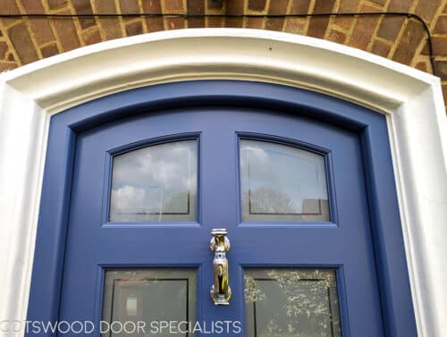 arched Georgian front door painted blue fitted into a brick house. Door and frame are both Accoya wood and painted blue. Banham high security locks. All door hardware polished chrome. Sandblasted glass with Clear inset border, double glazed. Closeup of arched door