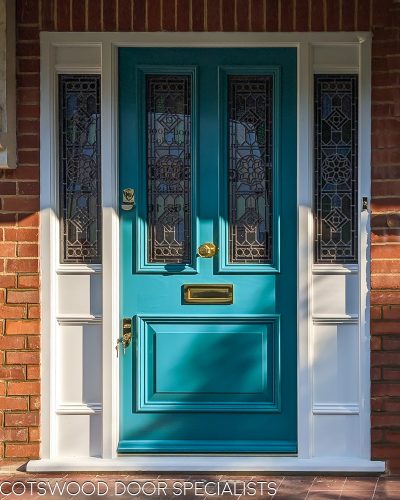 glazed Victorian front door with stained glass and a sidelight frame also with stained glass. Door and frame glass sizes carefully calculated to be the same size. Bespoke stained glass design with a star motif and vibrant primary colours. Door is vibrant turquoise green and haspolished brass furniture. Draught proofed and insurance rated high security banham locks fitted. Fitted in brick london home.