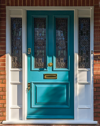 glazed Victorian front door with stained glass and a sidelight frame also with stained glass. Door and frame glass sizes carefully calculated to be the same size. Bespoke stained glass design with a star motif and vibrant primary colours. Door is vibrant turquoise green and haspolished brass furniture. Draught proofed and insurance rated high security banham locks fitted. Fitted in brick london home.