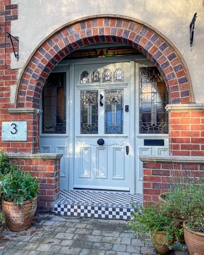light green elaborate Victorian front door with stained glass. Bespoke stained glass design. Door is light green and has black door furniture. Draught proofed and insurance rated high security banham locks fitted. Fitted in a red brick arch. The wooden door frame has side panels with stained glass and also a transom with stained glass. The bespoke wooden accoya door has 6 glazed panels and decorative mouldings