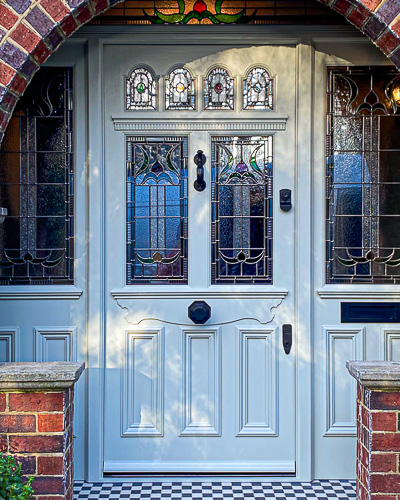 light green elaborate Victorian front door with stained glass. Bespoke stained glass design. Door is light green and has black door furniture. Draught proofed and insurance rated high security banham locks fitted. Fitted in a red brick arch. The wooden door frame has side panels with stained glass and also a transom with stained glass. The bespoke wooden accoya door has 6 glazed panels and decorative mouldings